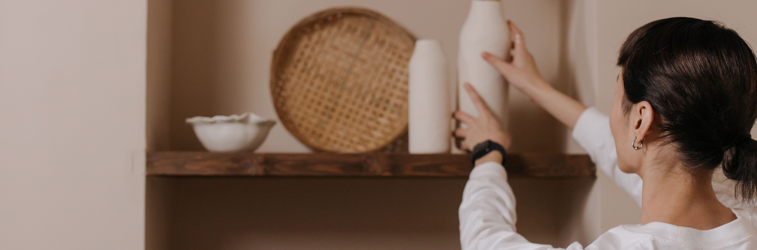 Person arranging a vase with dried plants on a shelf in a home setting